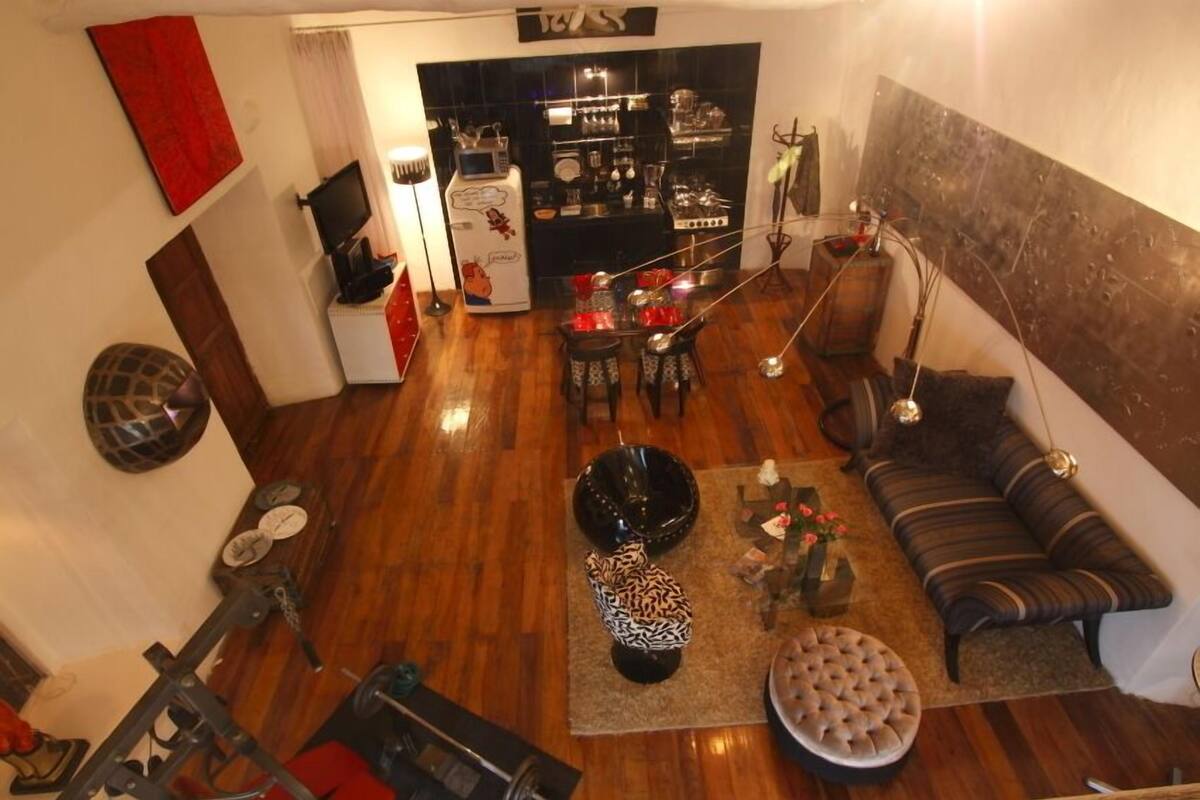 A spacious living area with a wooden floor, a sofa, a dining table, and a kitchen in the background.