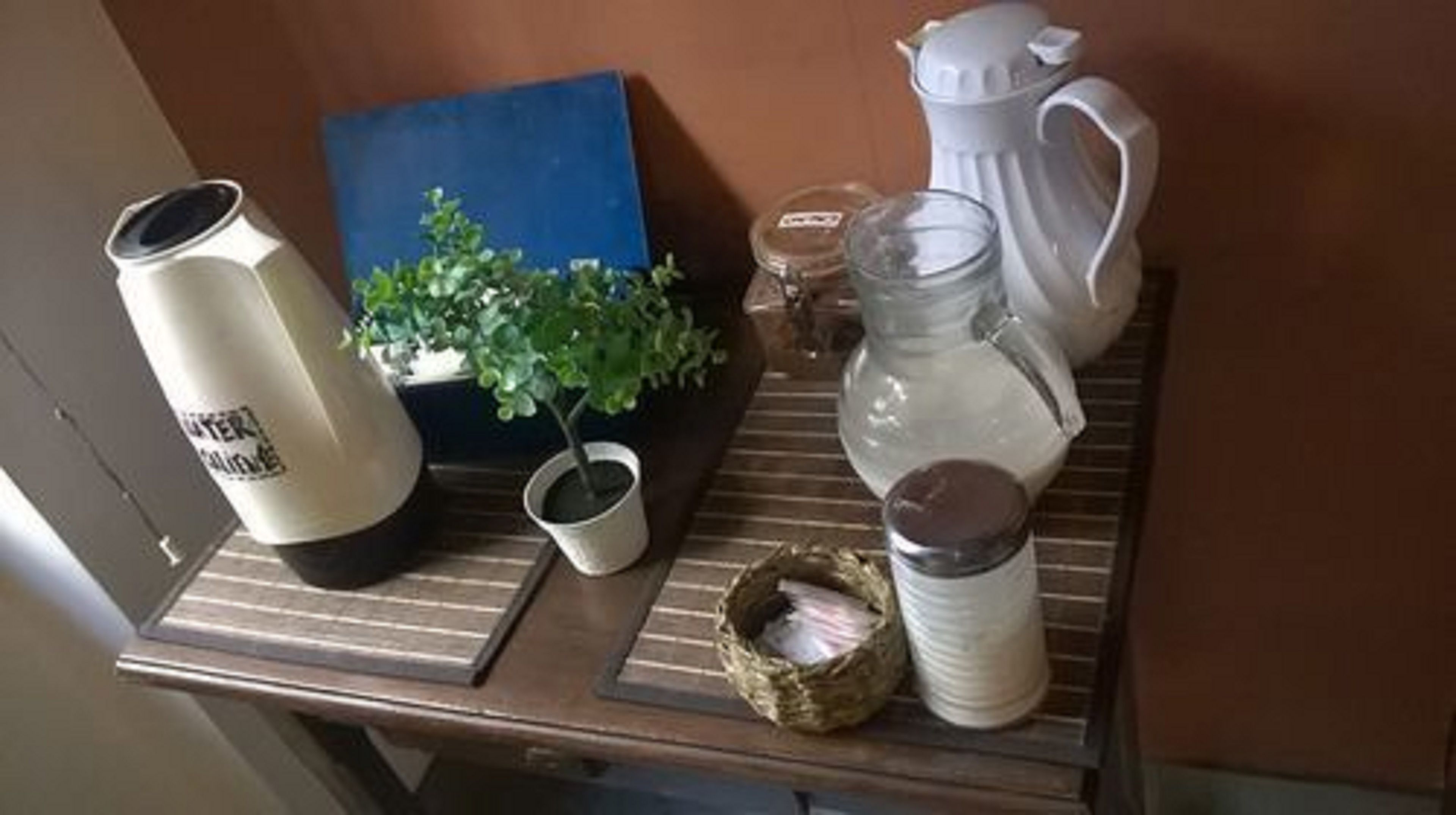 Uma bancada de cozinha com uma cafeteira, um pote, uma caneca e uma planta em vaso.