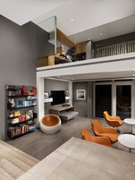A modern living room with a flat-screen TV, bookshelves, and orange chairs.