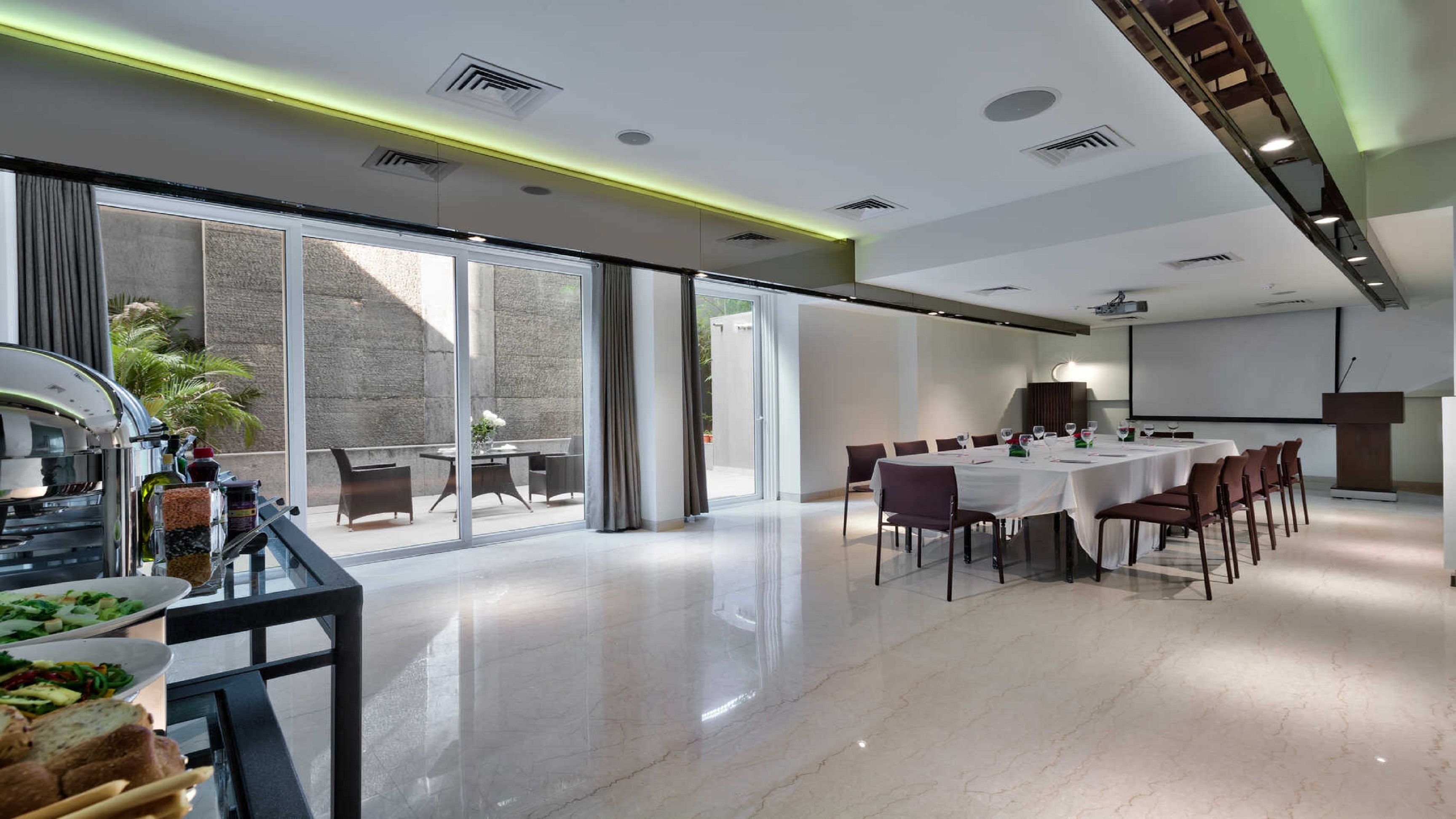 A modern conference room with a large table, chairs, a projector screen, and a presentation podium.