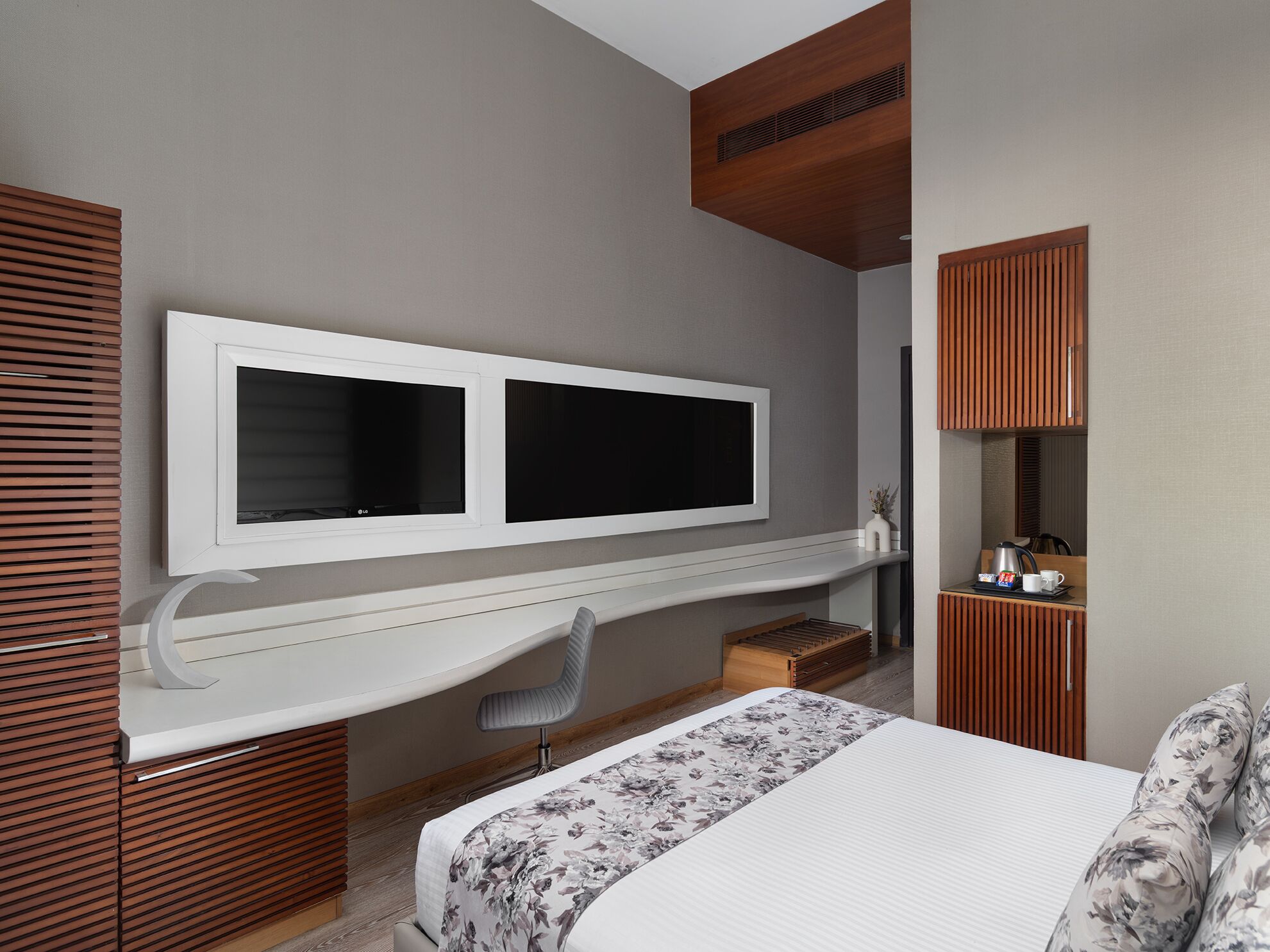 Une chambre moderne avec un grand lit, un bureau doté d’un téléviseur à écran plat et une coiffeuse avec un miroir.