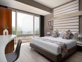 A modern hotel room with a large bed, a desk, and a view of the outdoors.