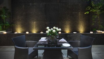 A table set for two with a vase of white flowers, candles, and a textured wall in the background.