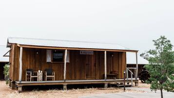 Een rustiek houten gebouw met veranda, twee stoelen, een kleine tafel en een bordje met de tekst 'Nile Hotel'.