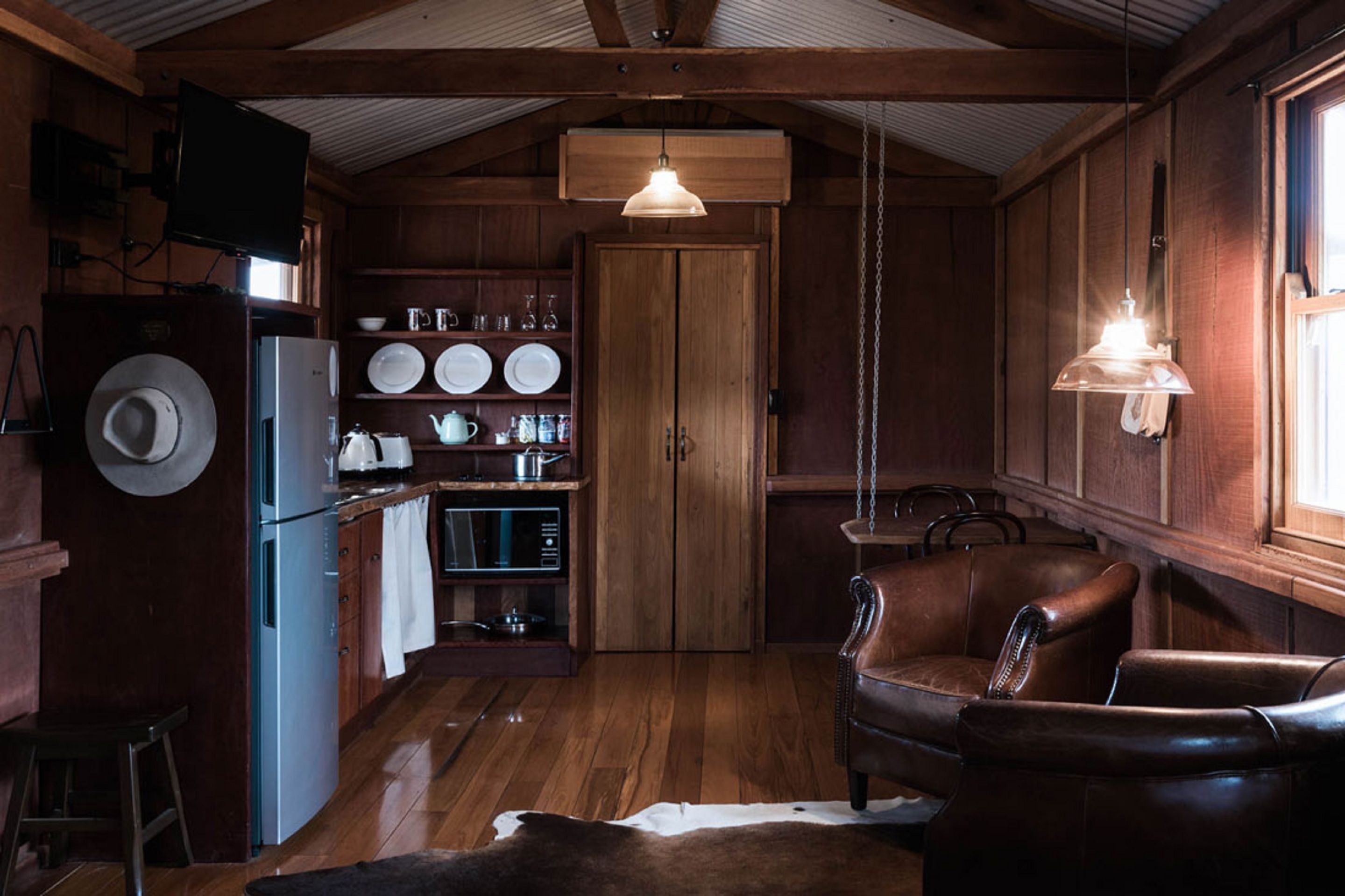 A rustic kitchen with wooden walls, a refrigerator, a dining table, and a leather chair.
