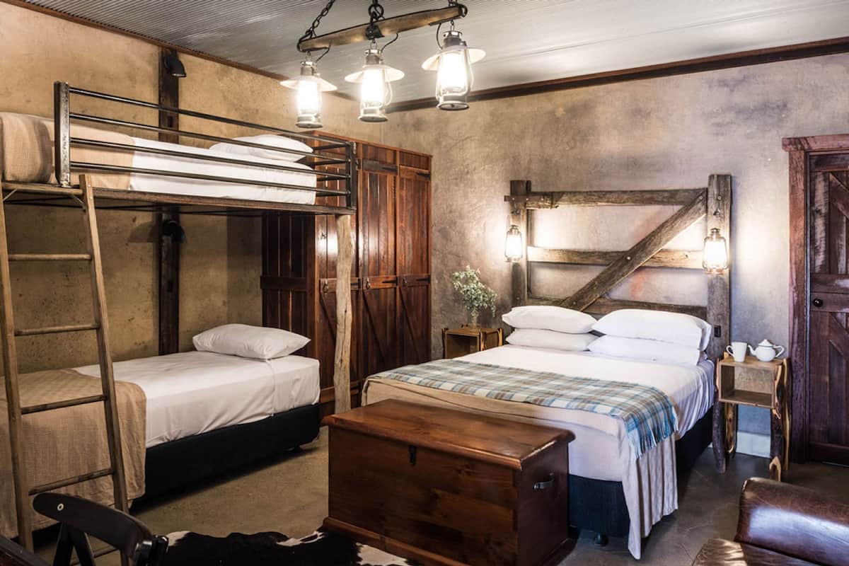 A rustic room with bunk beds, a wooden chest, and a small table with a lamp.