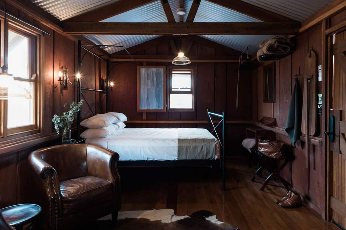 A rustic wooden room with a bed, leather chair, and a cowhide rug.
