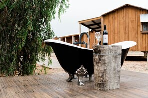 Una terraza de madera con una bañera negra, un cubo de madera y una botella de vino.