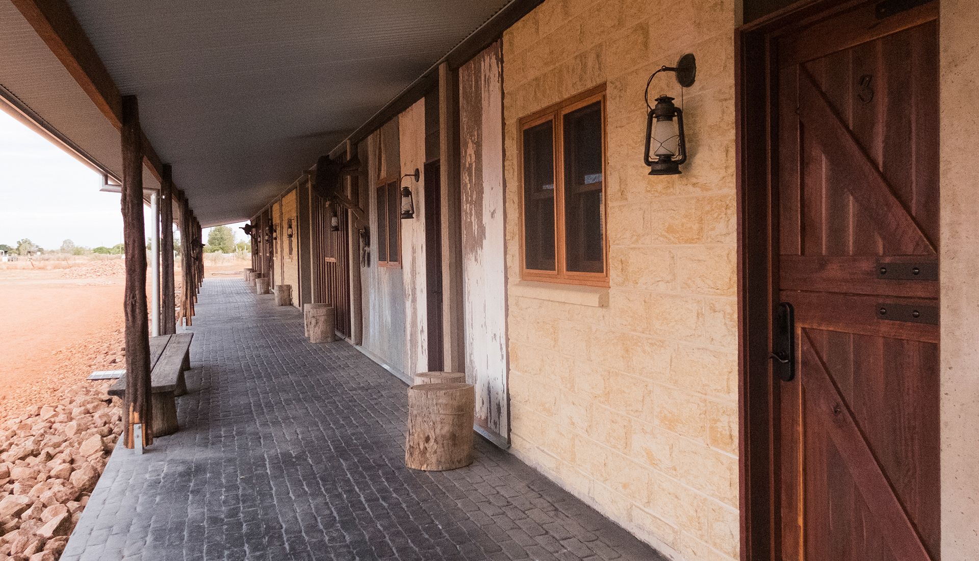 Un passadís cobert amb portes i finestres de fusta, un paviment de maons i pilars de pedra.