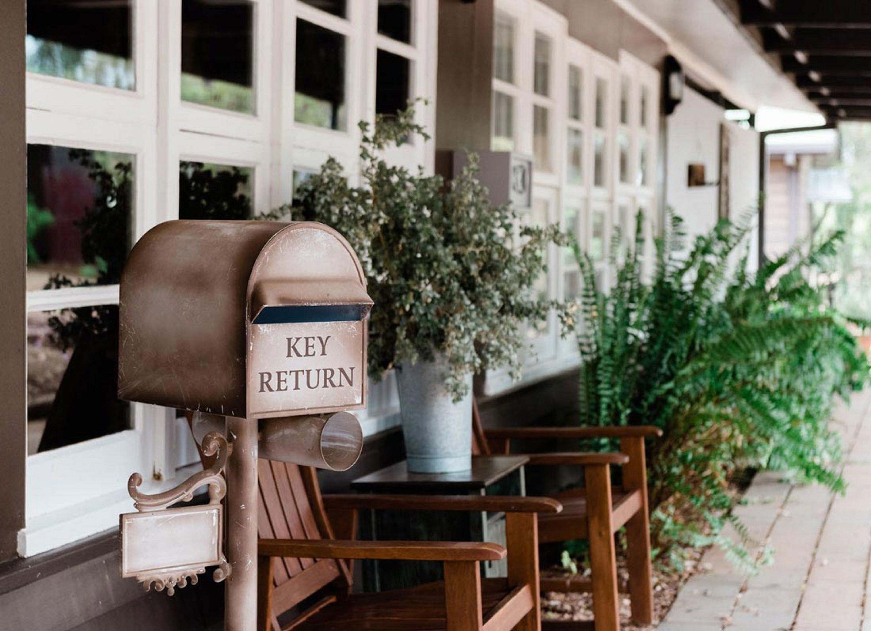 A mailbox labeled "KEY RETURN" on a porch with wooden chairs and a potted plant.
