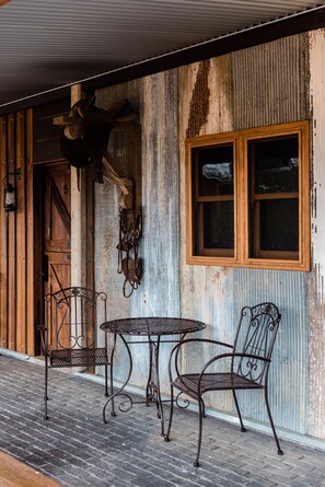 Un edificio rústico de madera con revestimiento de metal corrugado, una puerta de madera y una ventana. Hay una mesa de metal y dos sillas afuera.