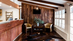 Un espace d’accueil avec un mur en bois, deux fauteuils en osier, une petite table avec une plante et un grand tapis.