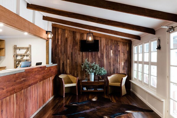 A reception area with a wooden wall, two wicker chairs, a small table with a plant, and a large rug. - Saltbush Retreat (Longreach)