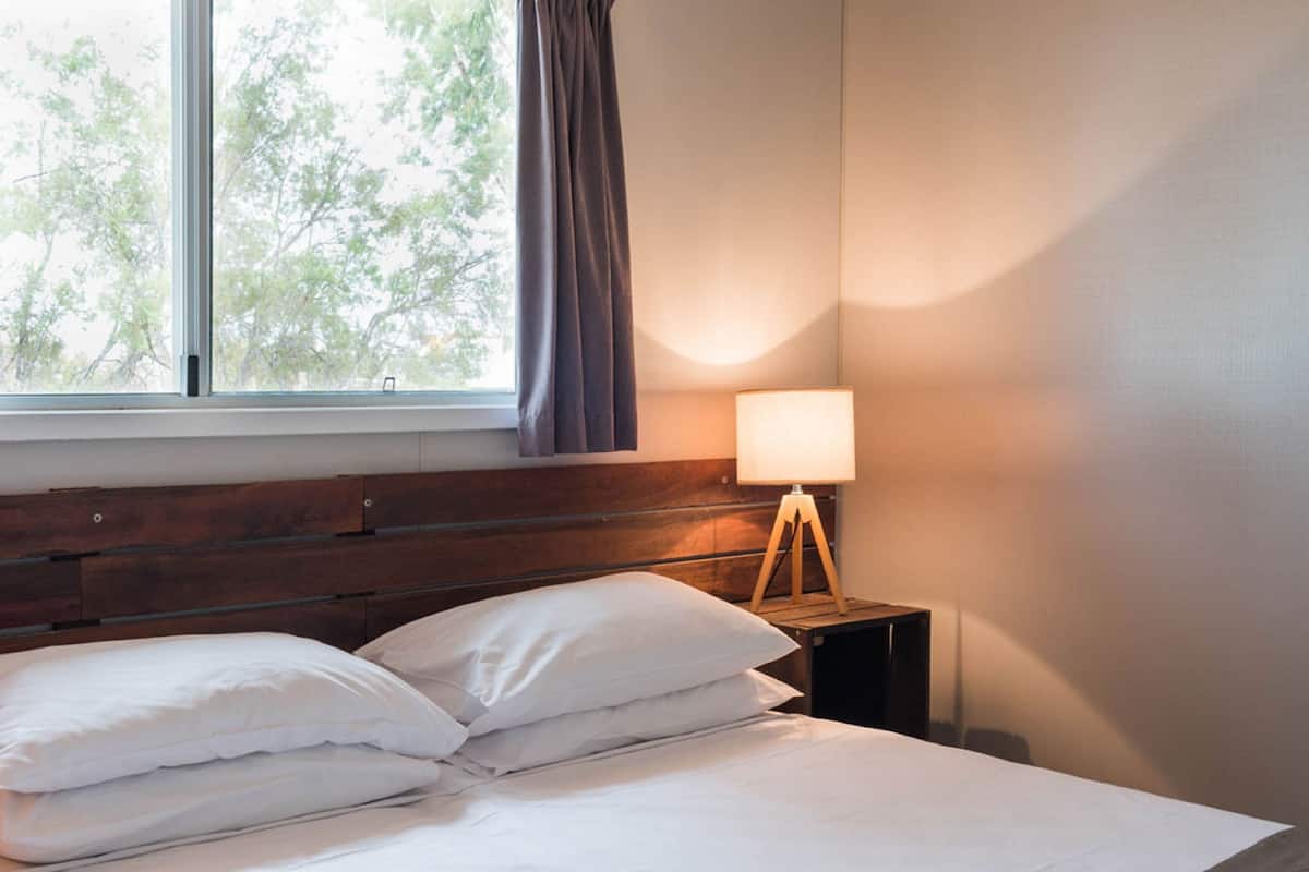 A neatly made bed with white linens, a wooden headboard, and a bedside lamp on a small wooden nightstand.