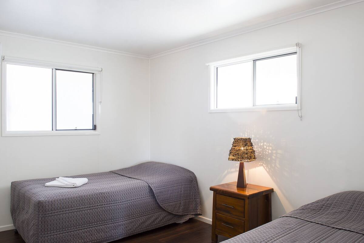 A bedroom with two beds, a nightstand, and a lamp.