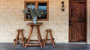 Un bâtiment rustique en pierre, doté d’une porte et d’une fenêtre en bois, d’une lanterne en métal et d’une table en bois accompagnée de deux tabourets.