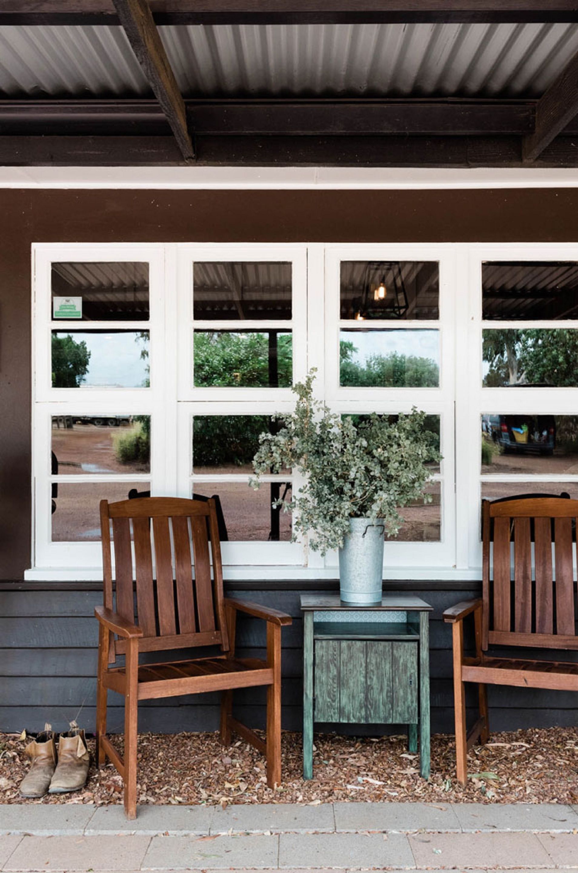 A covered outdoor seating area with two wooden chairs, a small table, and a vase with flowers.