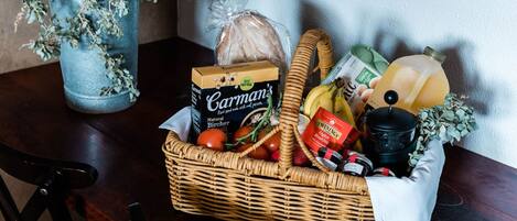 A wicker basket filled with groceries, including bread, tomatoes, and a bottle of juice, on a wooden table.