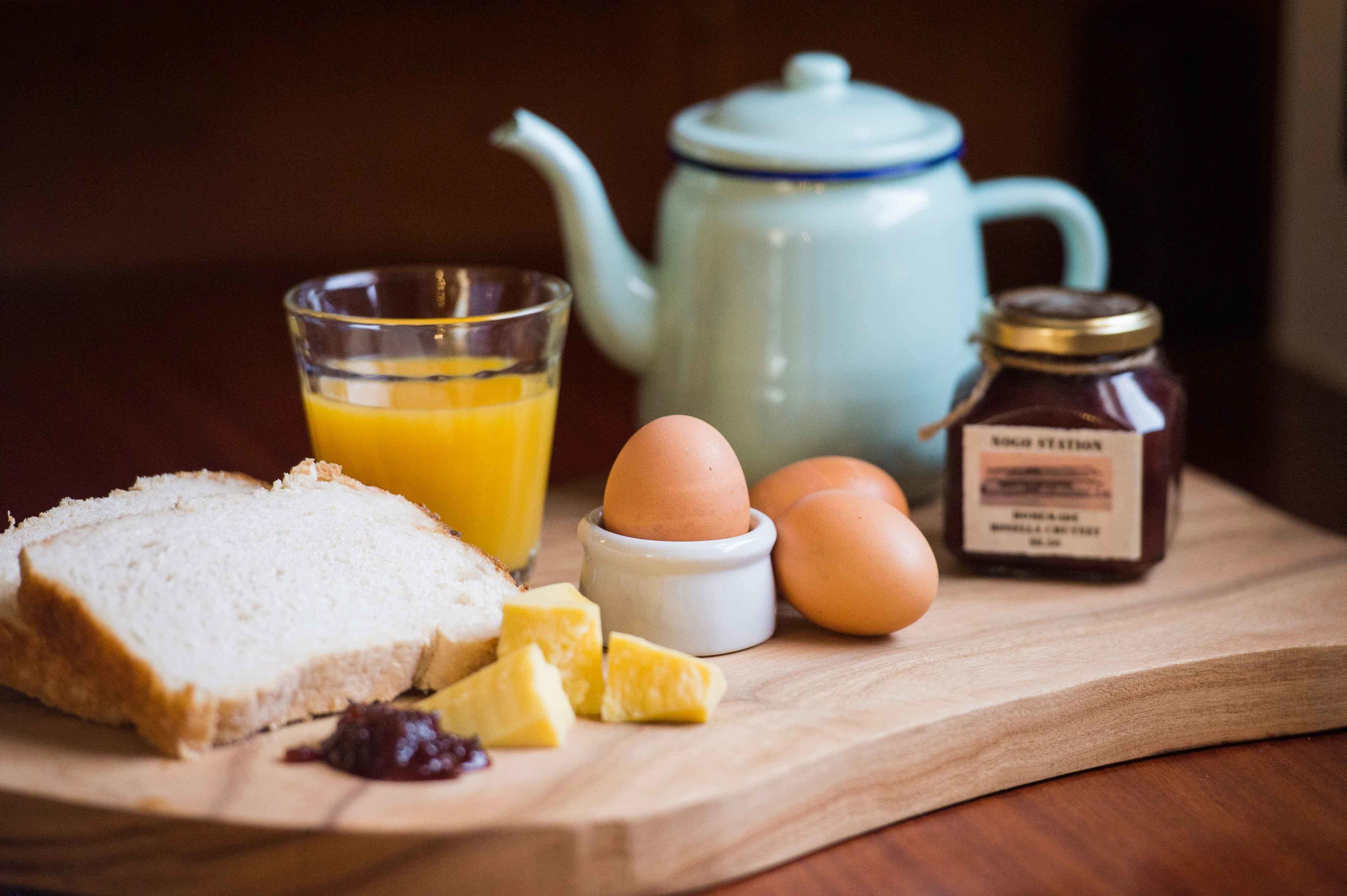 A breakfast setup with bread, eggs, butter, jam, and a teapot on a wooden board.