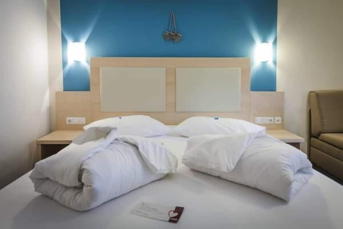 Hotellihuone, jossa on suuri sänky, kaksi yöpöytää ja sininen tehosteseinä.