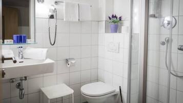 Ein modernes Badezimmer mit Waschbecken, Toilette und Dusche in Weiß. Auf dem Waschtisch steht ein kleiner weißer Hocker und ein Blumentopf.