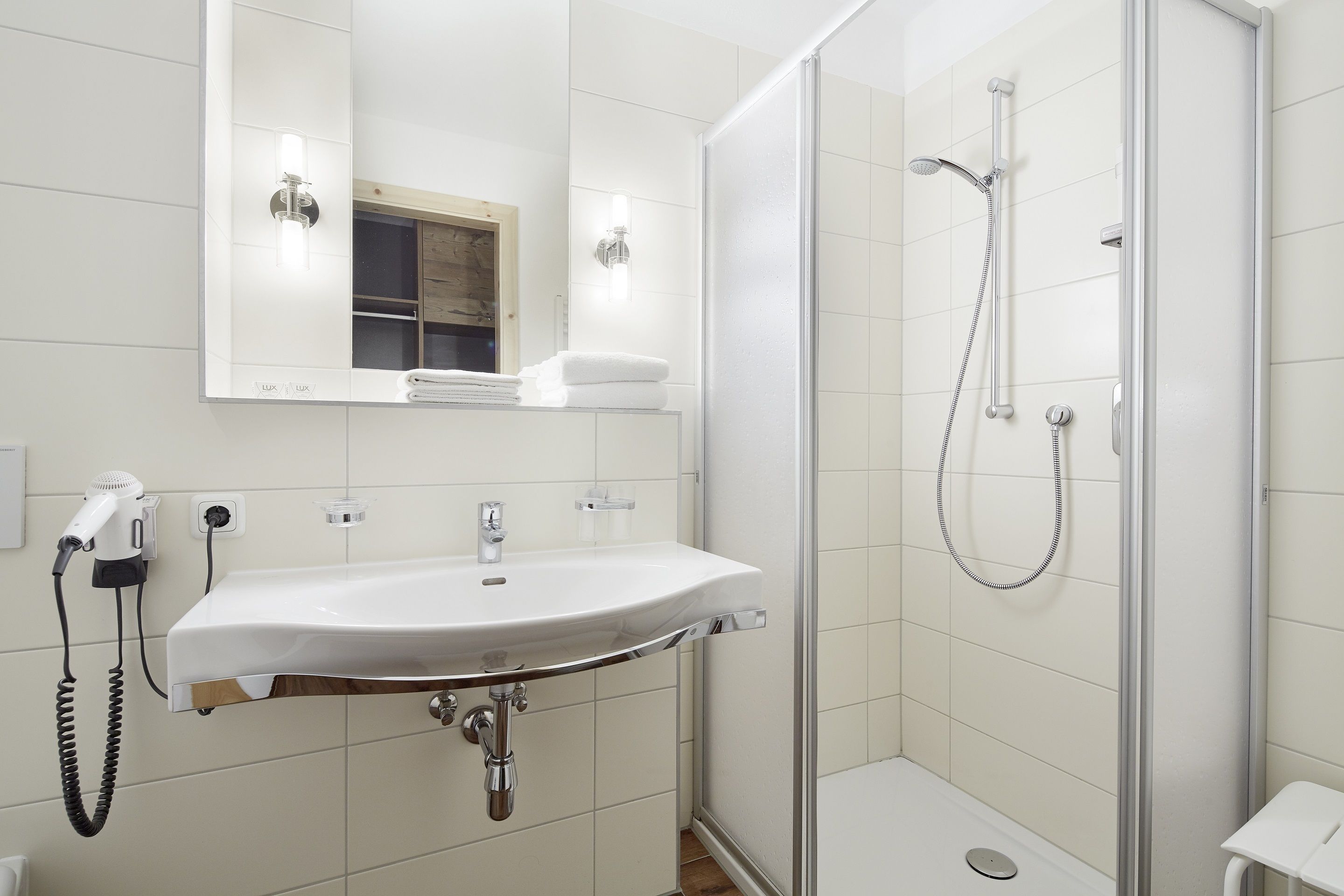 Une salle de bain moderne avec un lavabo blanc, un miroir et une douche à parois de verre.