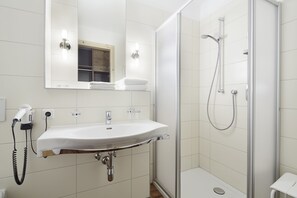 A modern bathroom with a white sink, a mirror, and a glass-enclosed shower. - Gasthof Salzstadl (Reutte)