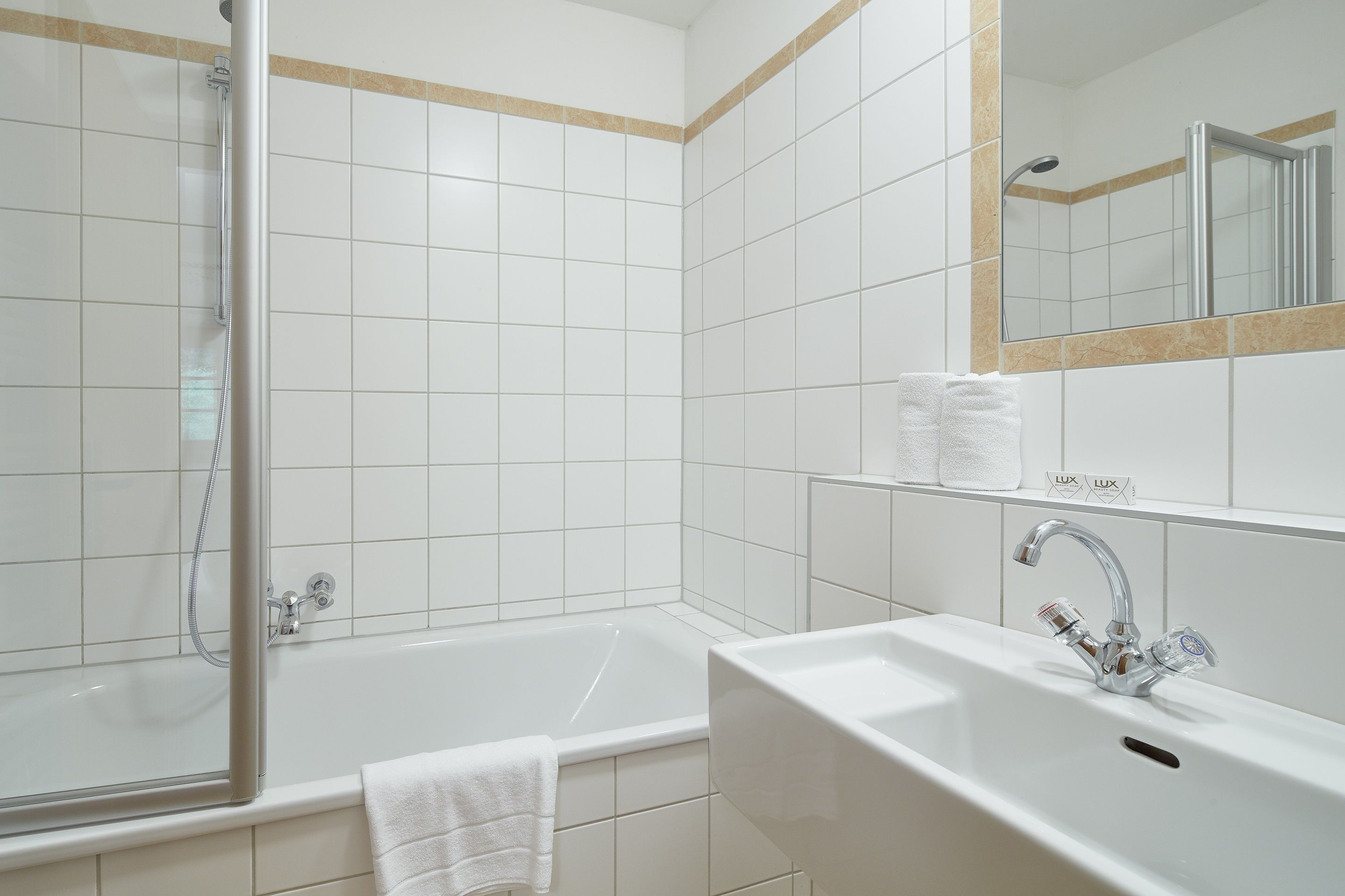 Ein modernes Badezimmer mit einer begehbaren Glasdusche, einer weißen Badewanne und einem Waschbecken mit Spiegel darüber.