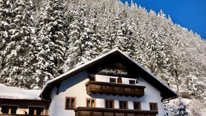 Un edificio de estilo alpino tradicional con un letrero que dice “Landgasthof Klaus”. Tiene un balcón de madera, múltiples ventanas y un paisaje nevado al fondo.