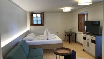 Una habitación pequeña con cama, una mesita, televisión y kitchenette.
