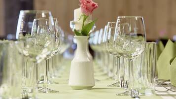Une table dressée avec plusieurs verres à vin et un vase blanc contenant une rose rose.