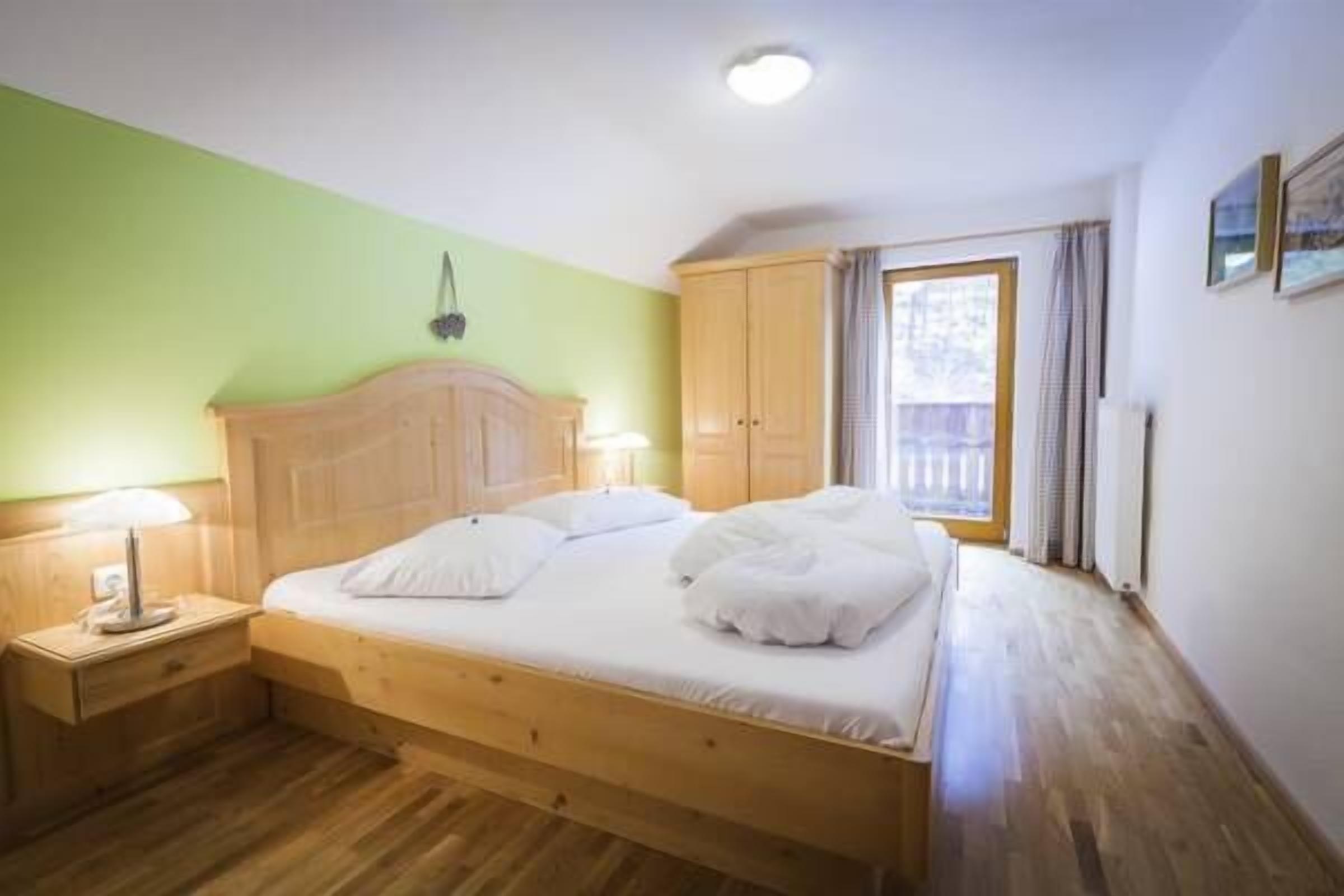Una cama individual con cabecera de madera, una mesita de noche con lámpara y una ventana con cortinas.
