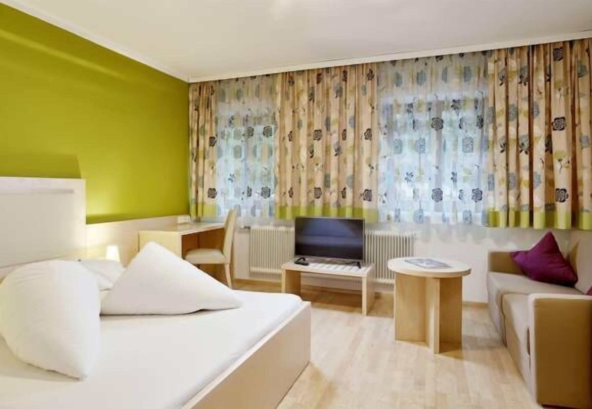 A hotel room with a bed, a desk, a television, and a sofa.