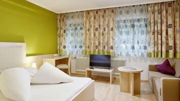 A hotel room with a bed, a desk, a television, and a sofa.