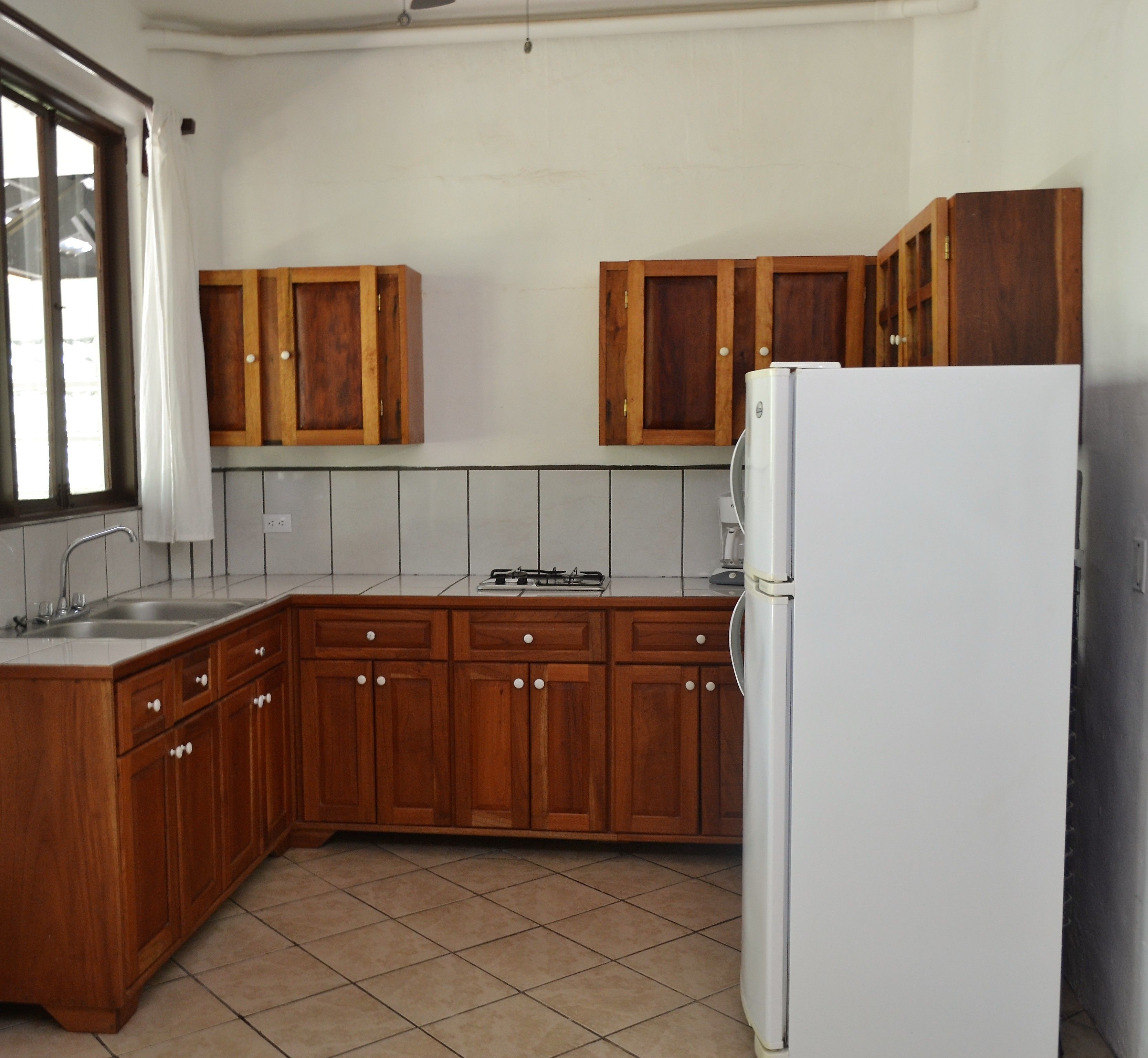 A kitchen with wooden cabinets, a white refrigerator, a sink, and a window with a curtain.