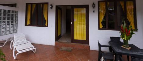 Un espacio al aire libre techado con una silla lounge blanca, una mesa con sillas y una planta en maceta.