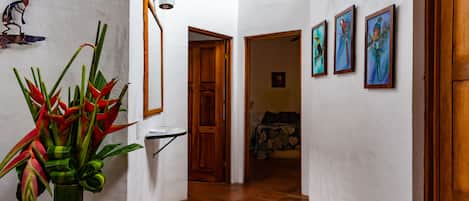 A hallway with a tiled floor, a wooden door, and a wall-mounted light fixture.