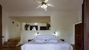 Un dormitorio con cama, ventilador de techo, mesita de noche, espejo y escalera.