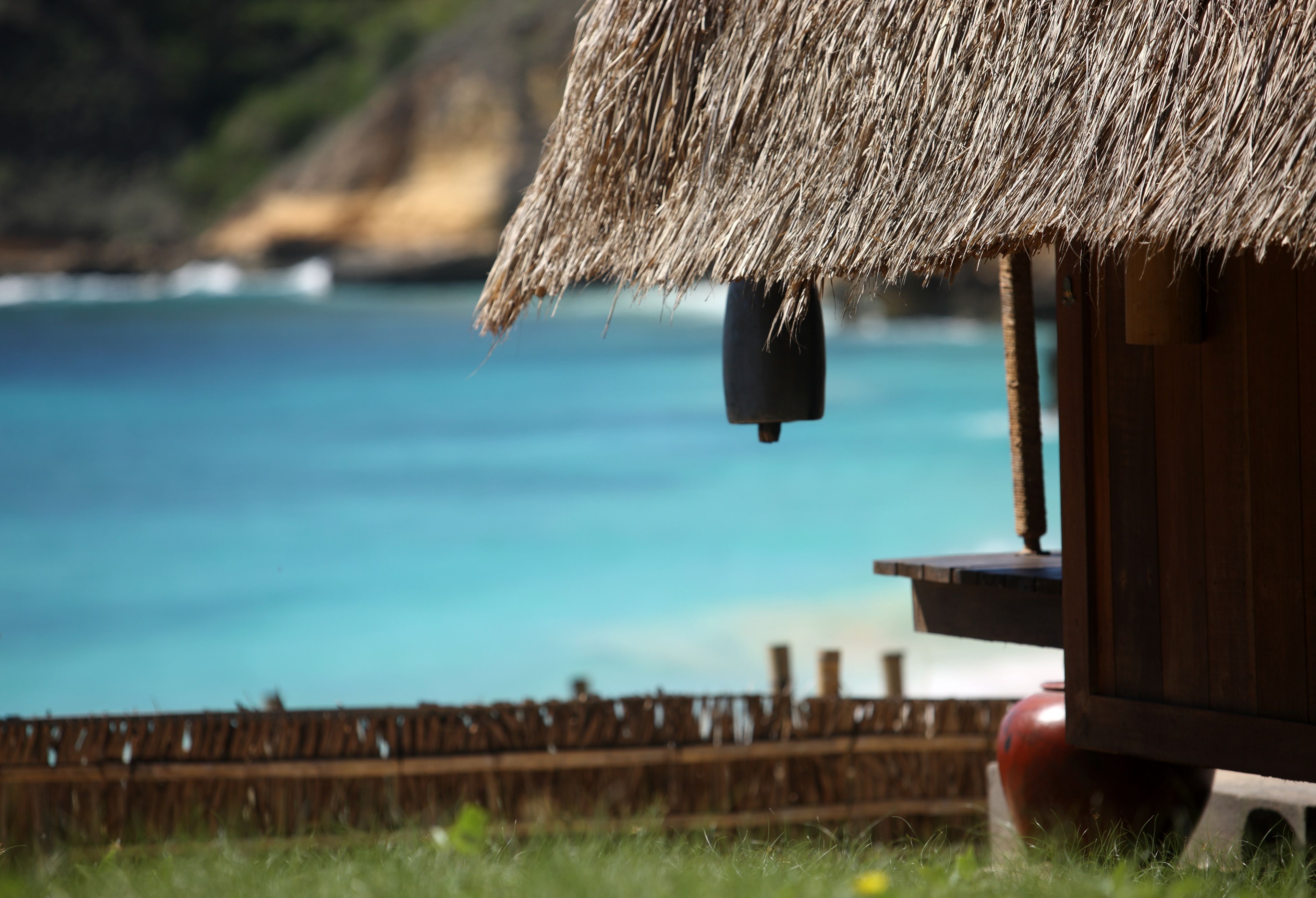A thatched-roof hut with a wooden structure, a red pot, and a view of the sea.