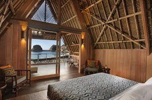 Quarto com cama grande, paredes de madeira e vista para o mar.