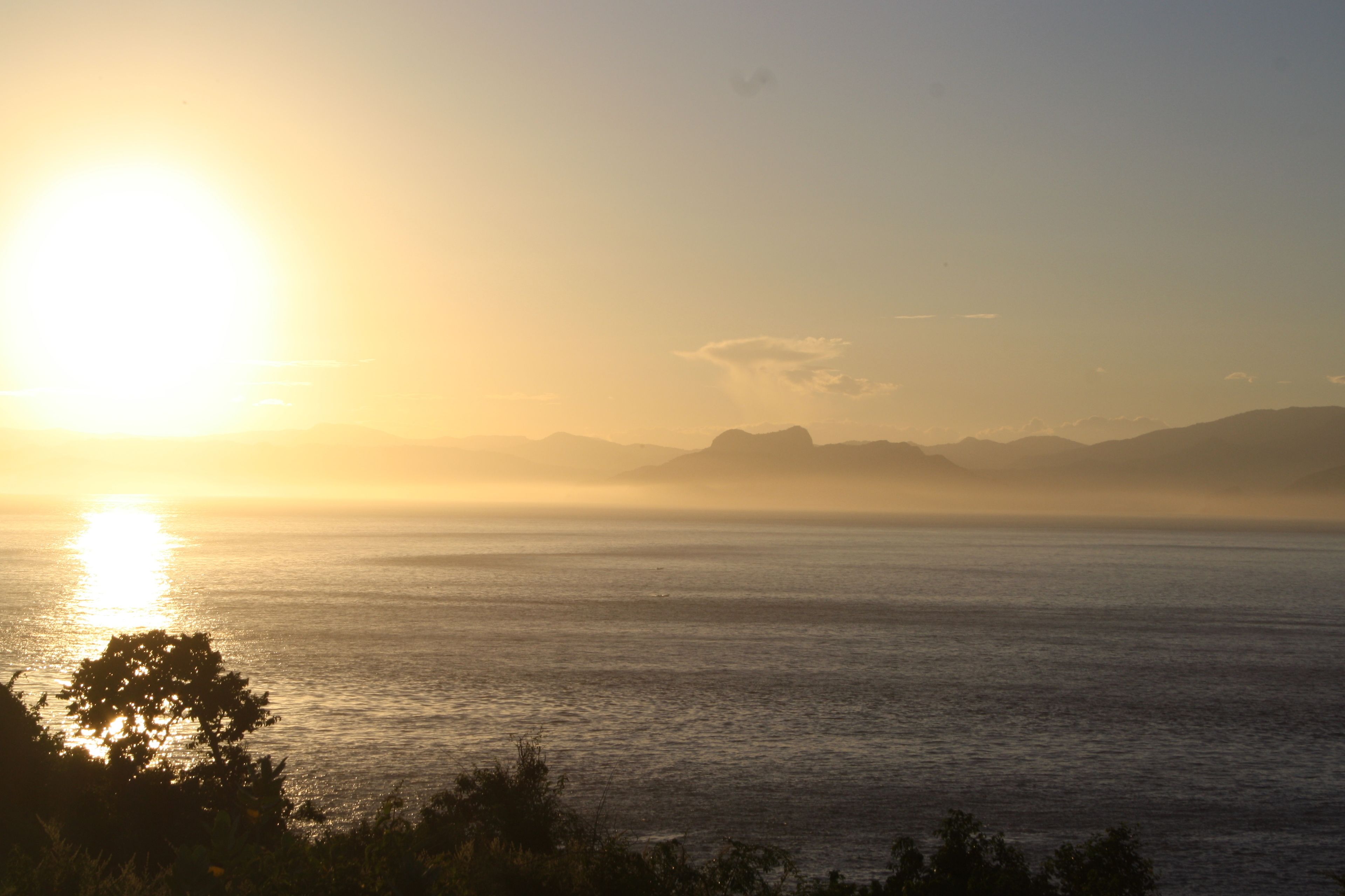 Una vista de la puesta de sol en la costa con montañas al fondo.
