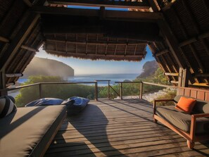 An outdoor deck with a view of the ocean, wooden furniture, and a thatched roof structure. - Jeeva Beloam Beach Camp (Jerowaru)