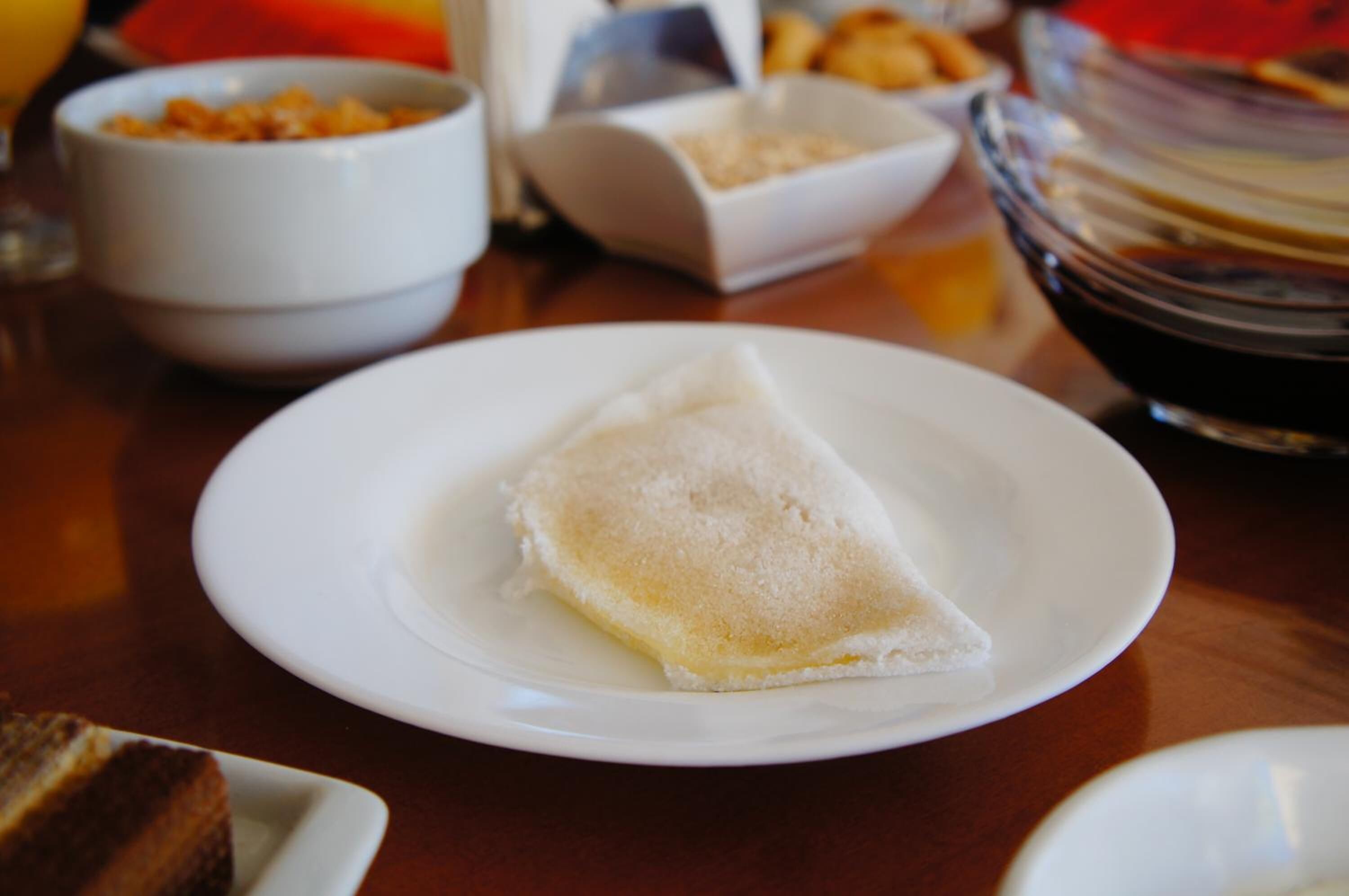A table with a plate of crepes, a bowl of cereal, and a glass of juice.