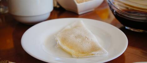 A table with a plate of crepes, a bowl of cereal, and a glass of juice.