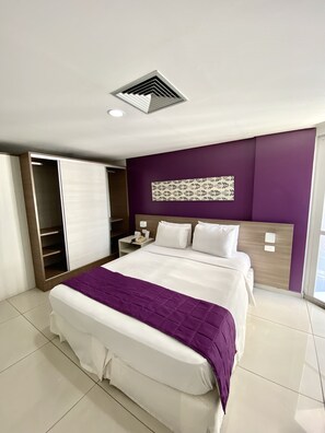 A modern hotel room with a large bed, a walk-in closet, and a decorative wall panel.