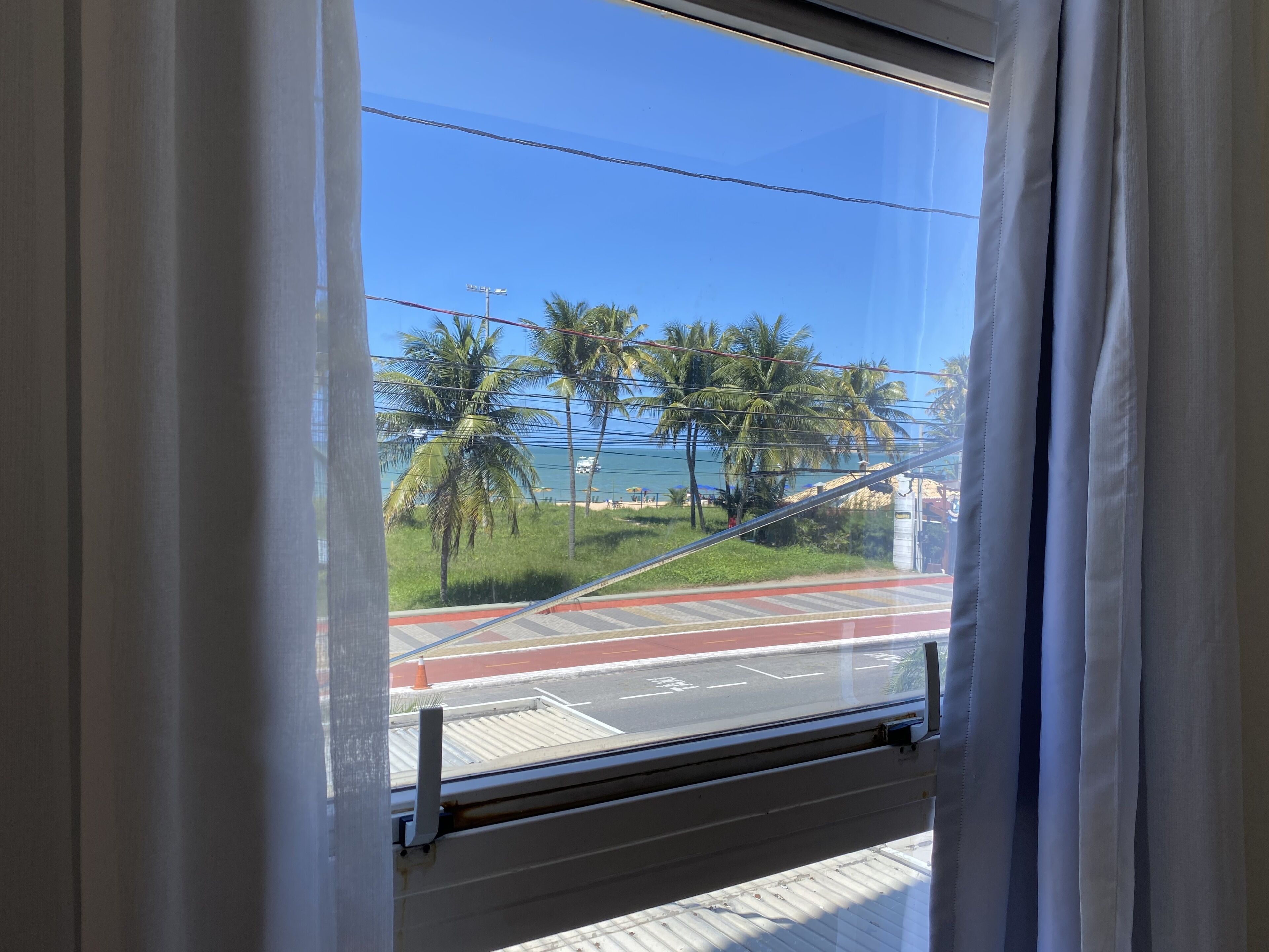A window with a view of a road, palm trees, and a clear blue sky.