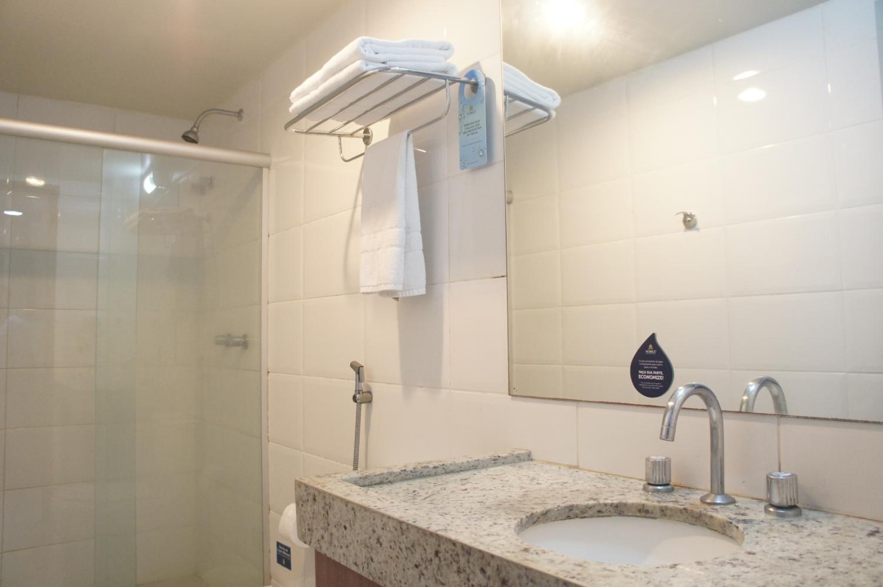 A bathroom with a glass shower enclosure, a granite countertop sink, and a towel rack with folded towels.