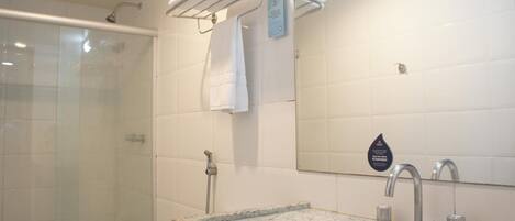 A bathroom with a glass shower enclosure, a granite countertop sink, and a towel rack with folded towels.