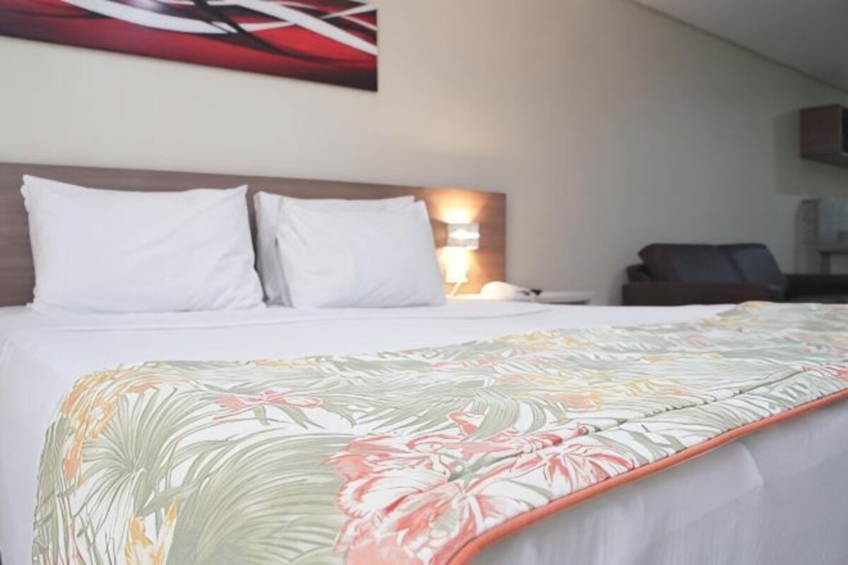 A neatly made bed with white linens, a floral-patterned blanket, and a headboard with a light fixture.