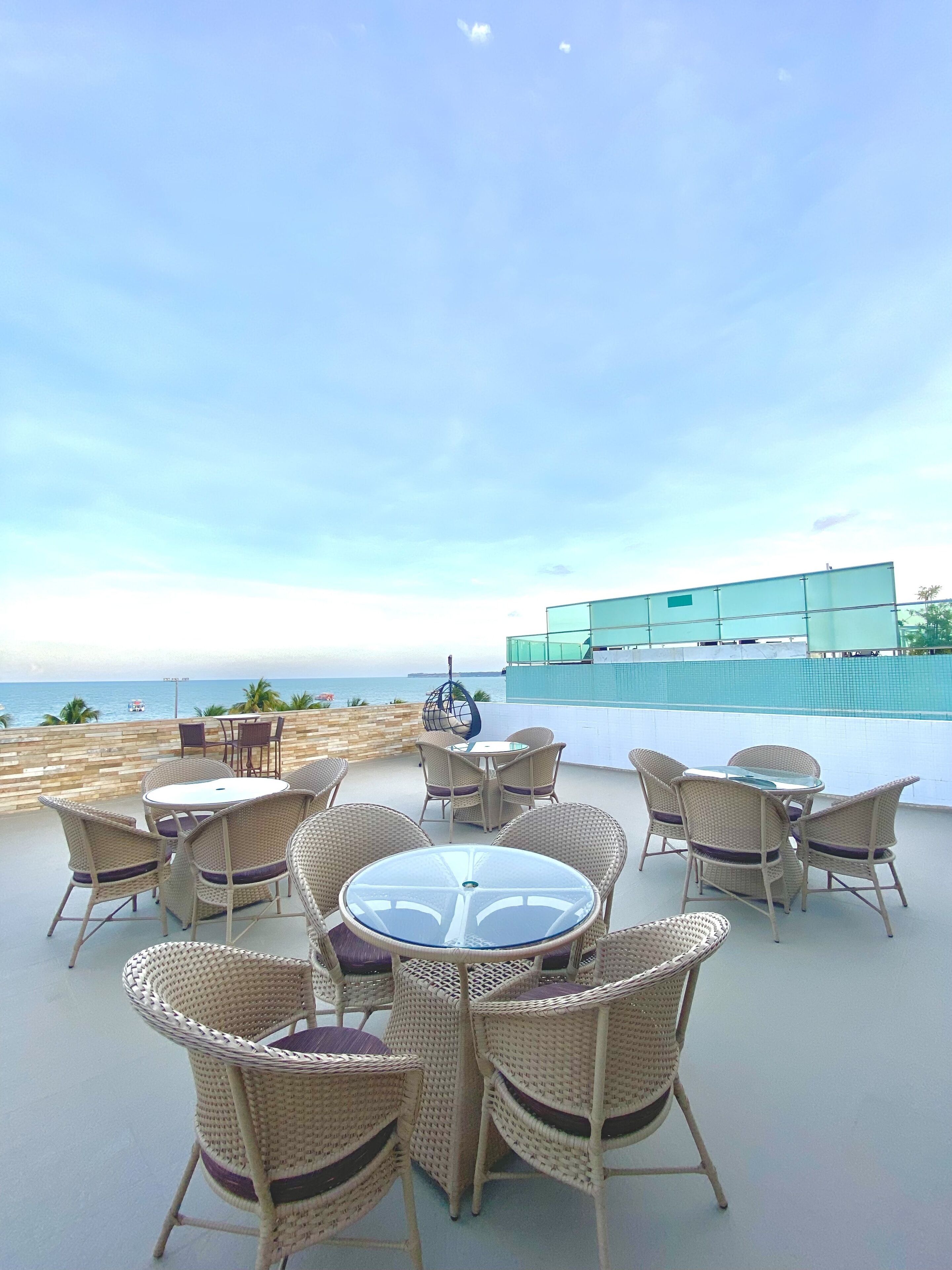 An outdoor seating area with wicker chairs and a glass table, overlooking a pool and the ocean.